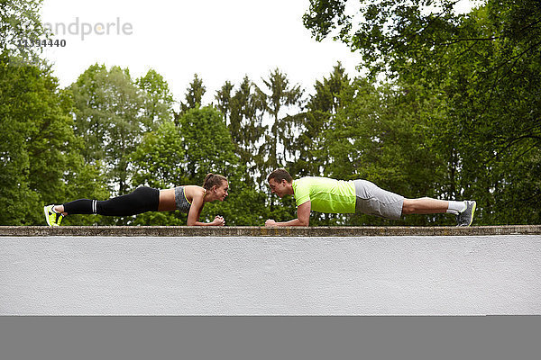 Ein junger Mann und eine junge Frau trainieren und machen Push-Ups gegenüberliegend auf der Mauer