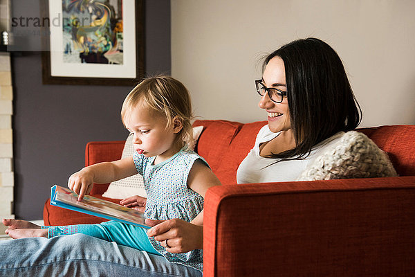 Mutter lehrt Tochter  das Buch auf dem Sofa zu lesen.