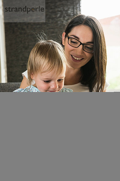 Mutter lehrt Tochter  das digitale Tablett zu Hause zu benutzen.