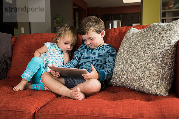 Geschwister mit digitalem Tablett auf dem Sofa