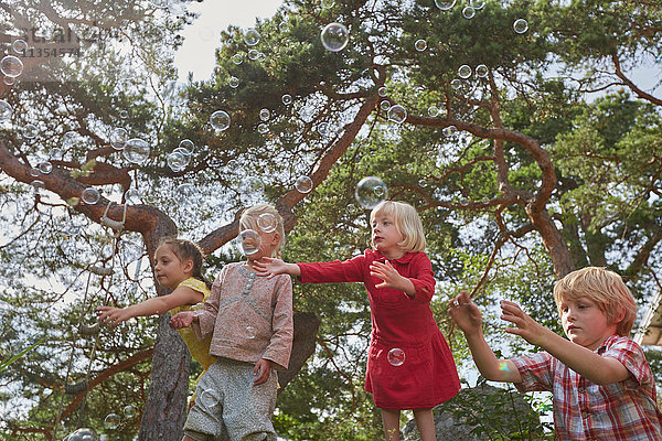 Kleine Gruppe junger Freunde spielt im Freien und beobachtet Luftblasen