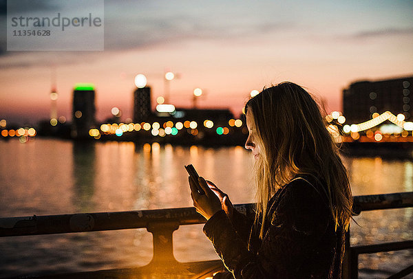 Junge Frau am Wasser  in der Dämmerung  mit Smartphone