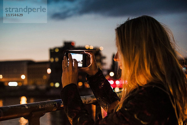 Junge Frau am Wasser  in der Dämmerung  fotografiert Ansicht mit Smartphone