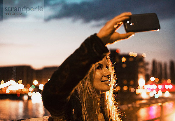 Junge Frau am Wasser  die sich mit einem Smartphone selbstständig macht