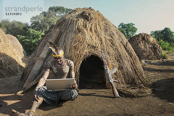 Mann des Mursi-Stammes mit Laptop und Kalaschnikow-Pistole  Omo-Tal  Äthiopien