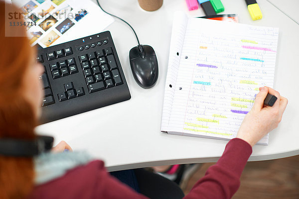 Junge Studentin am Computertisch beim Schreiben von Notizen