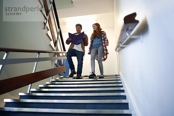 Junge männliche und weibliche College-Studenten bewegen sich die Treppe hinunter und lesen Akte