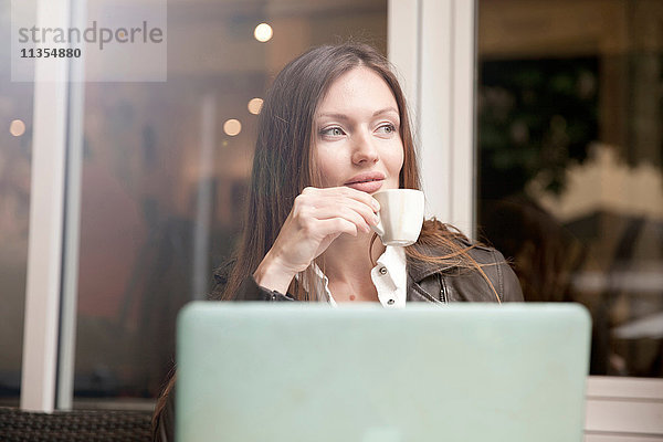 Geschäftsfrau mit Laptop trinkt Espresso im Straßencafé