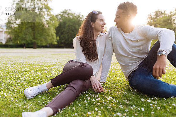 Junges Paar auf Gras sitzend  von Angesicht zu Angesicht lächelnd