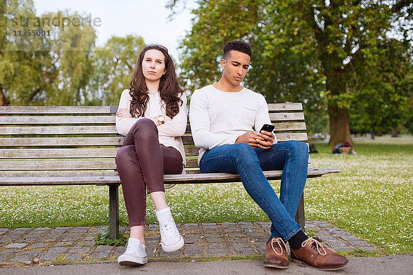Junges Paar auf Parkbank mit Smartphone