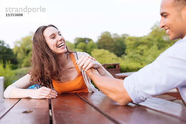 Lachendes junges Paar beim Armdrücken auf der Picknickbank