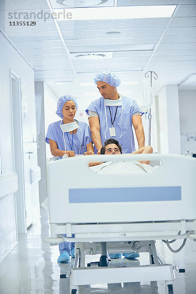 Ärzte in OP-Kleidung schieben Patient im Krankenhausbett
