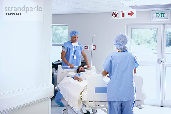 Ärzte in OP-Kleidung schieben Patient auf Krankenhausbett