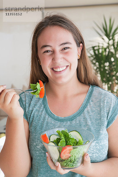 Teenager-Mädchen hält Salatschüssel und schaut lächelnd in die Kamera