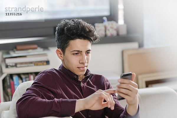 Junger Mann auf dem Sofa schreibt SMS auf Smartphone