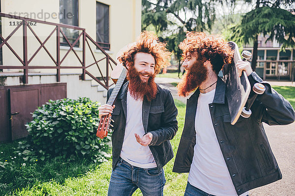 Junge männliche Hipster-Skateboarder-Zwillinge mit roten Bärten spazieren im Park