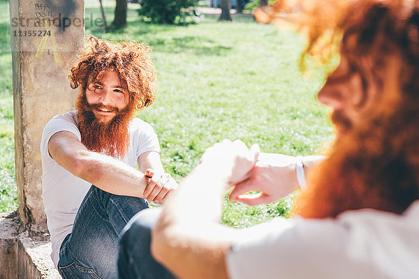 Junge männliche Hipster-Zwillinge mit roten Bärten auf Parkwand sitzend