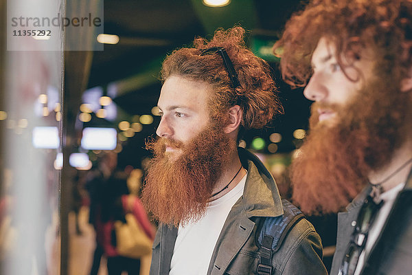 Junge männliche Hipster-Zwillinge mit roten Haaren und Bärten beim Schaufensterbummel bei Nacht