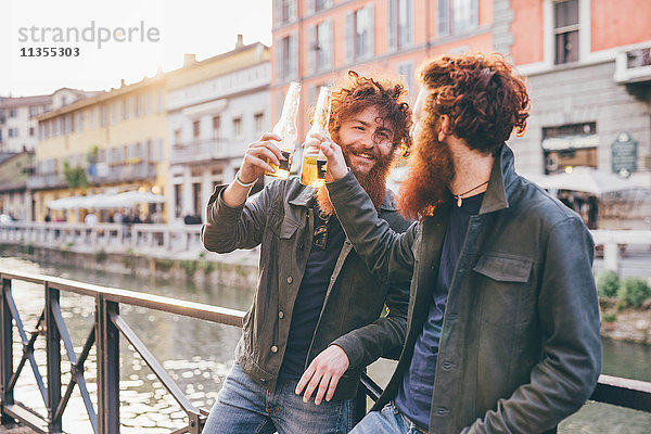 Junge männliche Hipster-Zwillinge mit roten Haaren und Bärten  die einen Toast am Kanalufer ausbringen.