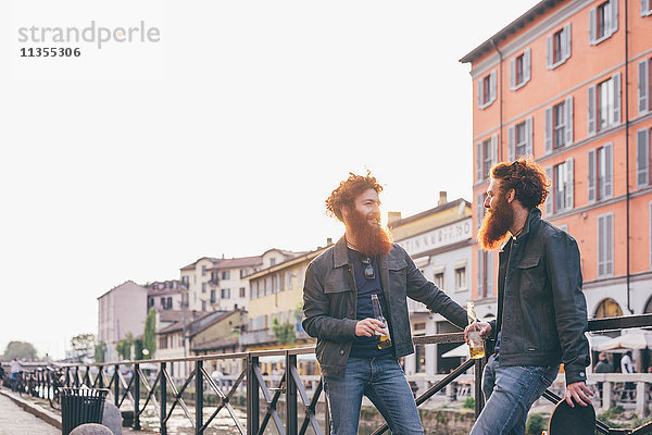 Junge männliche Hipster-Zwillinge mit roten Haaren und Bärten  die am Kanalufer sprechen.