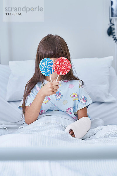 Porträt einer Patientin  die auf der Kinderstation eines Krankenhauses Lollipops vor die Augen hält