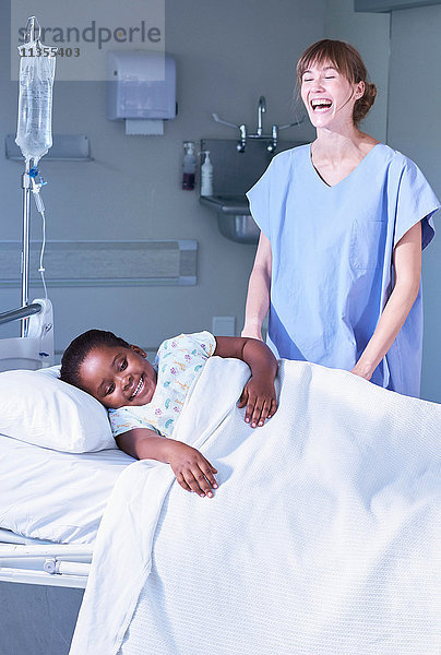 Krankenschwester lacht mit Patientin im Bett auf der Kinderstation des Krankenhauses