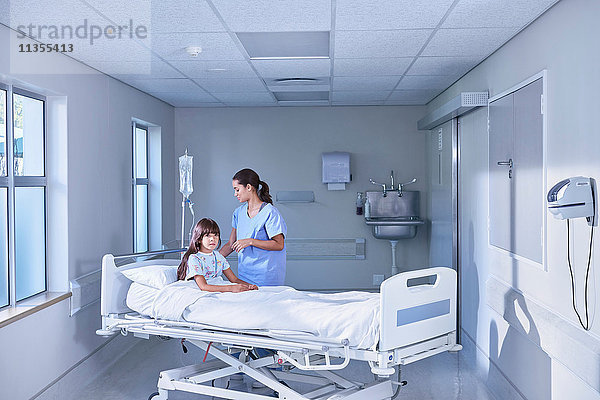 Krankenschwester  die den intravenösen Tropf für eine Patientin im Bett auf der Kinderstation des Krankenhauses einstellt