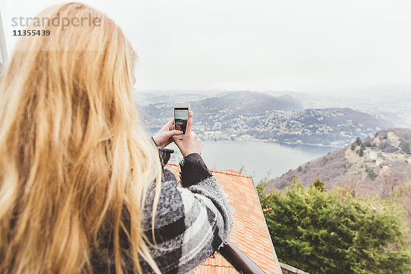 Junge Frau fotografiert den nebligen Comer See von der Dachterrasse aus  Italien