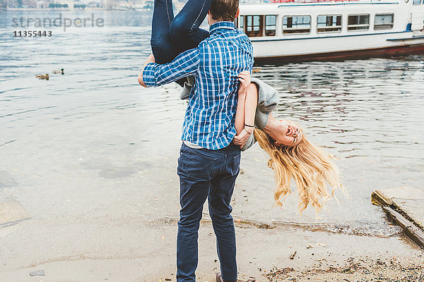 Junger Mann trägt seine Freundin kopfüber am Seeufer  Comer See  Italien