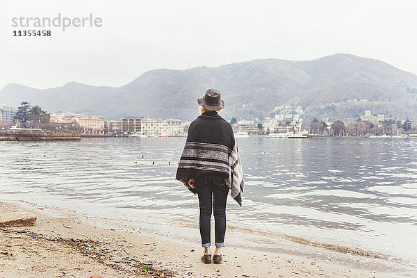 Rückansicht einer stilvollen jungen Frau  die vom Seeufer aus auf den Comer See schaut  Comer See  Italien