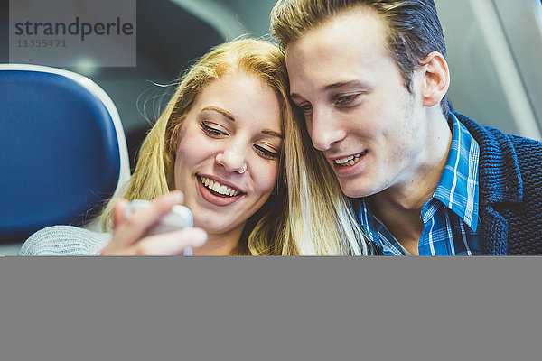 Junges Paar liest im Zugwaggon Smartphone-Texte