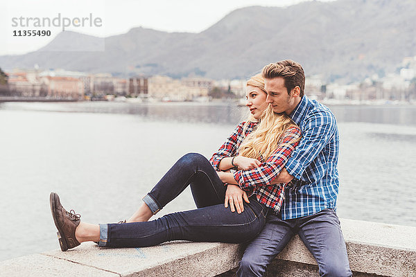 Romantisches junges Paar sitzt auf einer Hafenmauer  Comer See  Italien