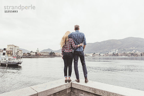 Rückansicht eines jungen Paares  das auf der Hafenmauer steht und hinaussieht  Comer See  Italien