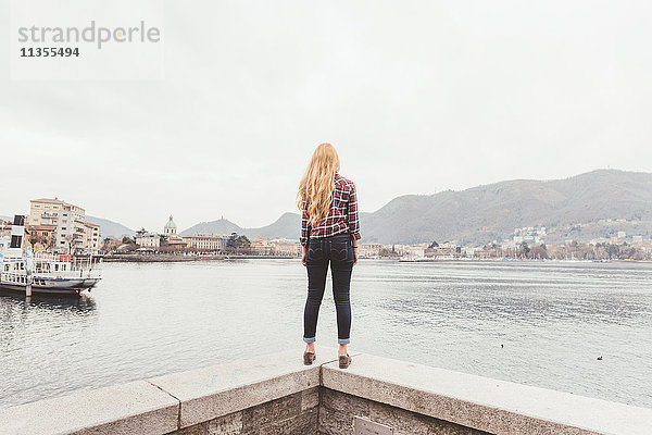 Rückansicht einer jungen Frau  die auf der Hafenmauer steht und nach draußen schaut  Comer See  Italien