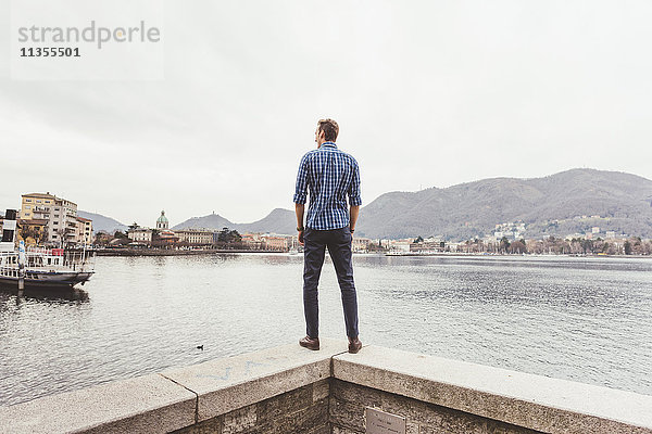 Rückansicht eines jungen Mannes  der auf der Hafenmauer steht und hinaussieht  Comer See  Italien