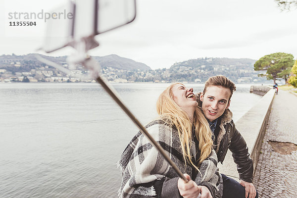 Lachendes junges Paar mit Smartphone-Selfie an der Hafenmauer  Comer See  Italien