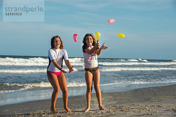 Zwei junge Schwestern spielen mit kleinen Luftballons am Strand