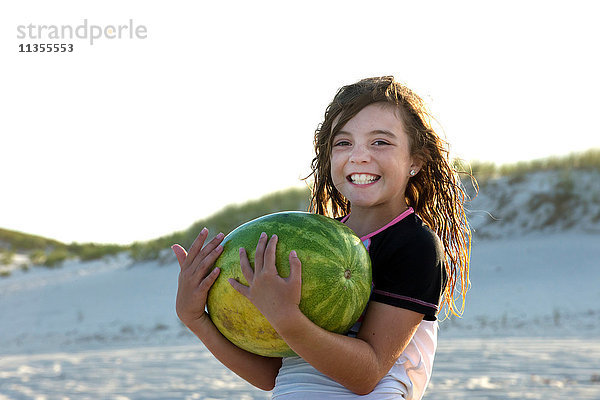 Porträt eines jungen Mädchens am Strand  das eine Melone hält und lächelt