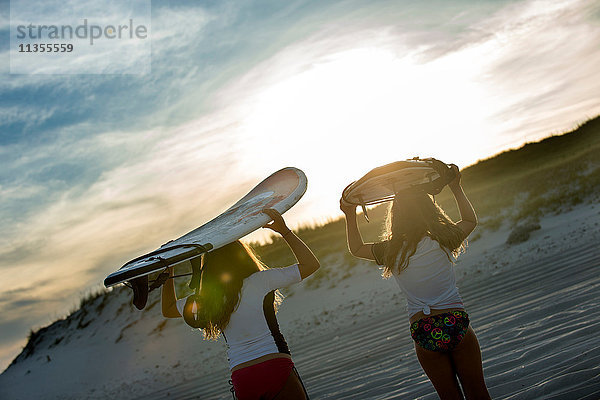 Zwei junge Mädchen im Meer  Surfbretter haltend  Rückansicht