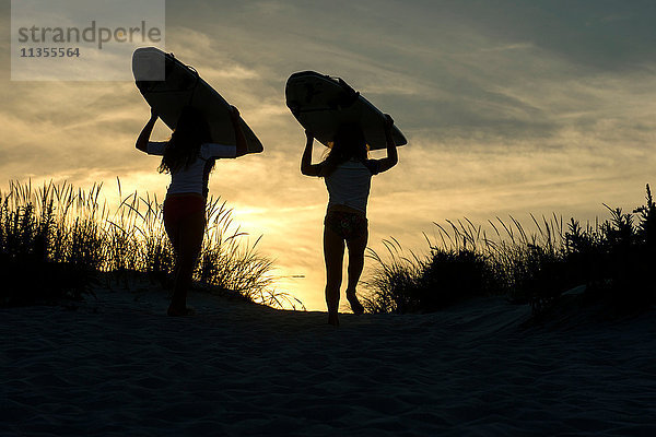 Zwei junge Mädchen auf Sanddünen  in der Abenddämmerung  mit Surfbrettern