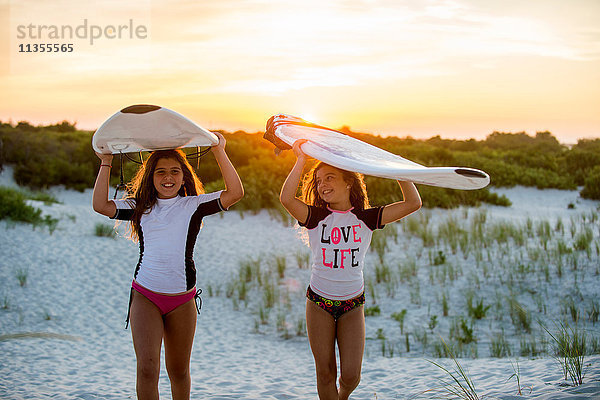 Zwei junge Mädchen am Strand  die Surfbretter tragen