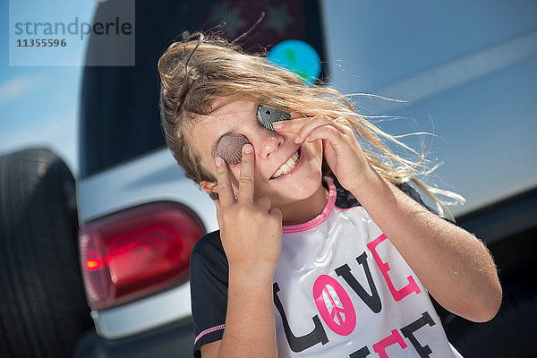 Porträt eines jungen Mädchens am Strand  die Augen mit Muscheln bedeckt  lächelnd