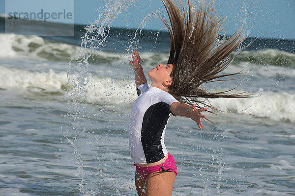 Junges Mädchen steht im Meer und schnippt mit nassem Haar