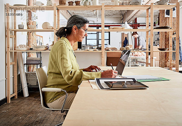 Seitenansicht einer Frau am Schreibtisch in einem Workshop mit Laptop