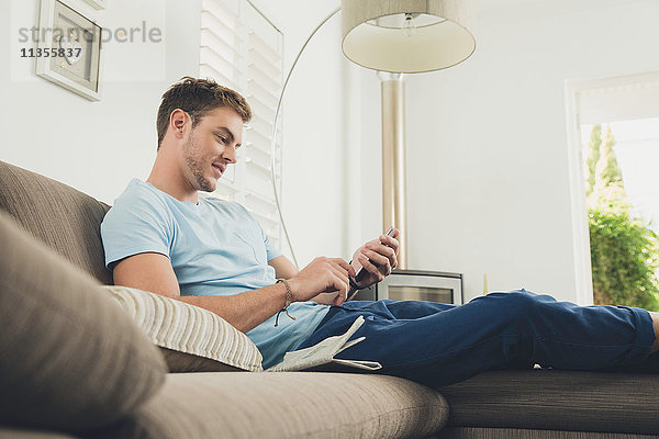 Mann auf Sofa schreibt lächelnd auf Smartphone