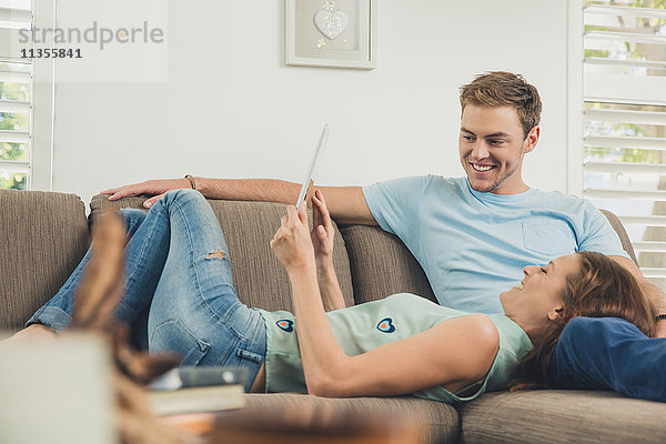 Paar entspannt auf dem Sofa mit digitalem Tablet lächelnd