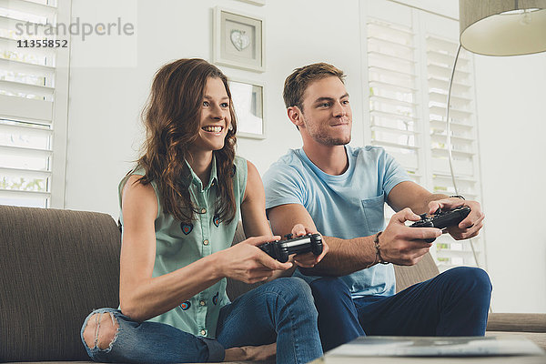 Paar auf dem Sofa mit Videospiel-Controller lächelnd