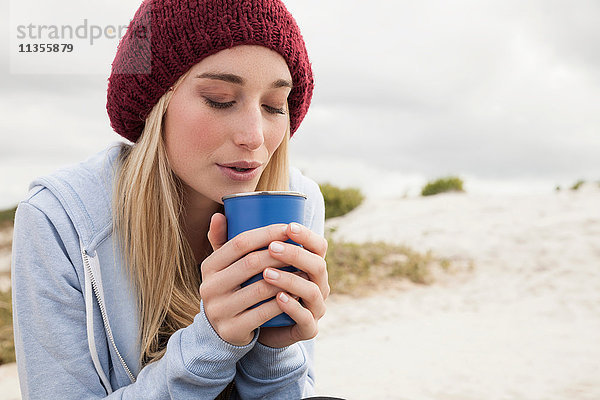 Junge Frau bläst an kaltem Tag in eine Tasse Kaffee