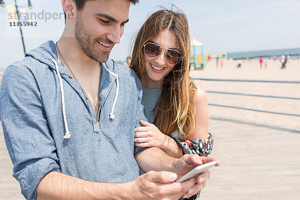 Paar betrachtet Smartphone lächelnd  Coney Island  Brooklyn  New York  USA