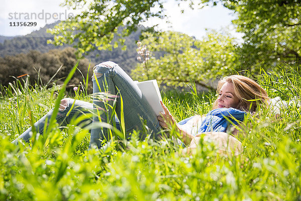 Frau liegt im Gras und liest